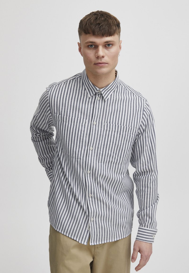 Camicia a righe in bianco e blu navy. Presenta un collo a camicia, due tasche sul petto e maniche lunghe. Realizzata in tessuto leggero.