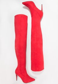 Røde over-knæ støvler lavet af ruskind med spidse tæer og høj stiletto-hæl. Glat tekstur med syninger langs skaftet.