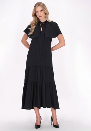 Robes maxi en chiffon noir avec un superposé style cape, décolleté en trou de serrure et ourlet à volants superposés. Associé à des talons aiguilles noirs.