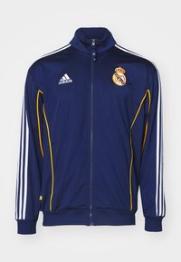 Veste de sport bleu marine avec des accents blancs et jaunes, dotée d'un col haut, d'une fermeture éclair complète et de trois rayures blanches sur chaque manche. Logos sur la poitrine.