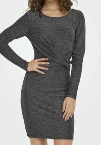 Robe noire à manches longues en tissu scintillant, avec une silhouette ajustée et un design torsadé au niveau de la taille. Texture lisse, longueur au genou.