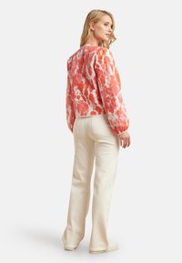 Bloemmotief, kort sweatervest in rood en wit met pofmouwen, gecombineerd met off-white flared pants en casual schoeisel.