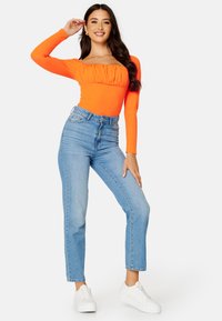 Oranje geribbelde langemouwen body met geplooide halslijn, gecombineerd met hooggetailleerde lichtblauwe rechte spijkerbroek en witte sneakers.