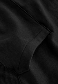 Tessuto in felpa nera, leggermente testurizzato. Presenta un orlo e polsini a costine, con un design della tasca senza cuciture e cuciture pulite.