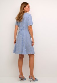 Abito a righe blu e bianche con maniche corte, vita aderente e gonna svasata. Il tessuto presenta una texture liscia. Abbinato a tacchi azzurri chiari.