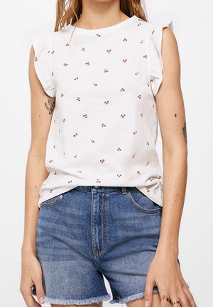 Hvid ærmeløs top med lille kirsebærprint og flæseærmer, båret med højtsiddende blå denimshorts med frynset kant.