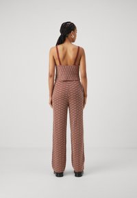 Combinaison en tissu avec un haut ajusté à fines bretelles, un motif texturé rouge et blanc, et des pantalons larges, vue de dos.