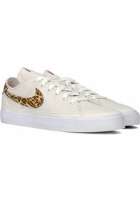 Zapatillas de lona blancas con un swoosh en estampado de leopardo en tonos beige y marrón texturizado. Presentan un diseño con cordones y suelas de goma.