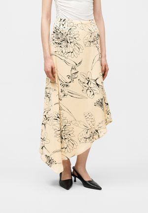 Μπεζ ασύμμετρη midi φούστα με μαύρο σκίτσο λουλουδιών, συνδυασμένη με μαύρα πέδιλα slingback και λευκό αμάνικο τοπ.