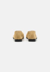 Beige karvase tekstuuriga loafersite tagumine vaade, mustade kulumiste ja õmbluste aksessuaaridega. Minimalistlik disain ümarate kujundustega.