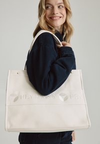 Canvas draagtas in crème met reliëfbranding "HEY MARLY HEY," met twee stevige handvatten en een minimalistisch ontwerp.