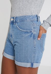 Jeansshorts i ljusblått med vikta uppvik, som har en klassisk design med fem fickor och en metallknapp vid midjan.