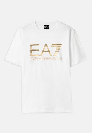 Camiseta de algodón blanca con un gran logo metálico dorado "EA7" y el texto "EMPORIO ARMANI" debajo, con mangas cortas y cuello redondo.