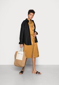 Casaco preto, vestido dourado e sandálias pretas. Bolsa bege com um painel branco e fecho. Texturas suaves e detalhes em botão.