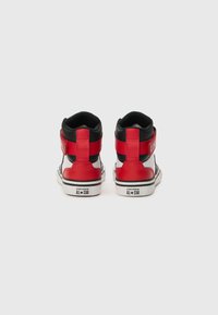 Punaiset ja mustat korkeavartiset tennarit valkoisilla pohjilla, joissa on nahkainen päällinen, pehmustettu kaulus ja ikoninen logo kantapäässä.