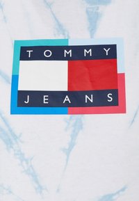 Tela de algodón blanca con un patrón de teñido anudado azul. El logo central presenta rectángulos rojos, blancos y azules con "TOMMY JEANS" en letras negras en negrita.