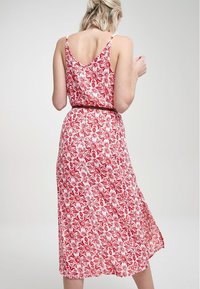 Robe à motifs floraux rouges avec une silhouette fluide et des bretelles spaghetti réglables. Fabriquée en tissu léger, avec une taille cintrée.