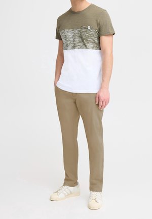 Pantalon kaki associé à un T-shirt à manches courtes avec un bloc de couleurs olive et blanc. Le T-shirt présente un devant texturé et une poche poitrine.