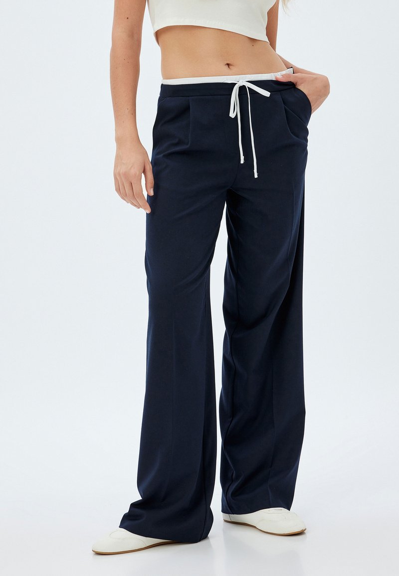 Pantalons larges bleu marine avec un cordon de serrage blanc à la taille et des poches avant, fabriqués à partir d'un tissu doux et léger, idéal pour le confort.