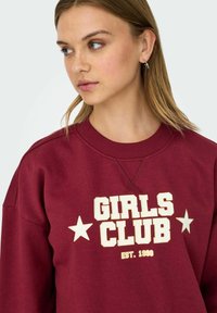 Maroon sweatshirt with ribbed collar, featuring "GIRLS CLUB" text and two stars in white, displayed prominently on the front.