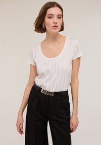 Hvid kortærmet t-shirt med lodrette striber og rund halsudskæring. Sammen med højtsiddende sorte bukser og et sort bælte med guld detaljer.