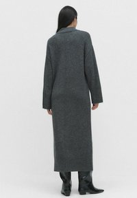 Lange grijze gebreide cardigan met een kraag, losse mouwen en geribbelde manchetten en zoom. Geschreven over zwarte, gemusterde enkellaarsjes.