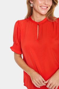 Blusa rossa con scollatura a oblò, maniche corte a sbuffo con dettagli arricciati e una morbida texture di tessuto leggero.