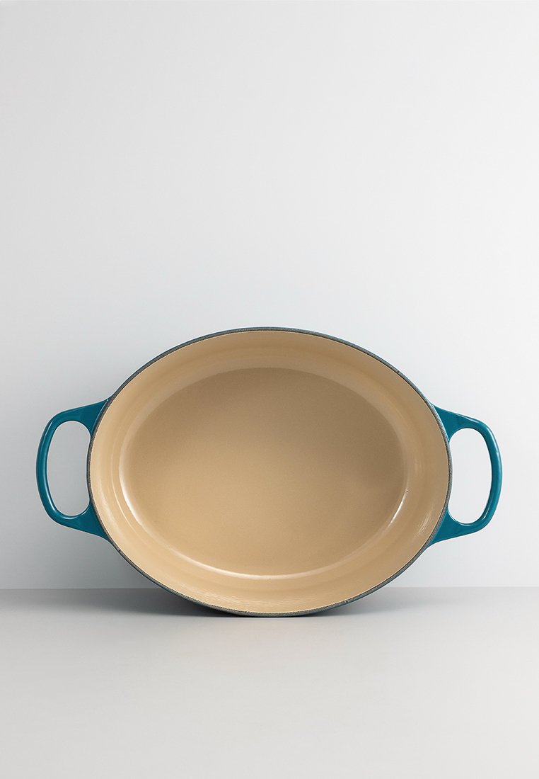 Ovale bakplaat met emaille coating en een beige binnenkant, teal handvatten en een gladde textuur; ontworpen voor veelzijdig koken en serveren.
