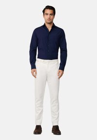 Camisa de vestido de color azul marino, diseño ajustado, con botones en la parte delantera, pantalones de algodón blancos, de pierna recta, y zapatos marrones. Estilo minimalista.