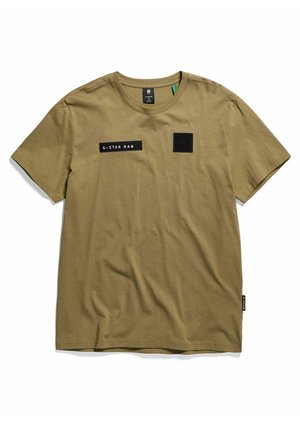 Oliwkowo-zielona bawełniana koszulka z krótkim rękawem i zaokrąglonym dekoltem, czarna metka G-Star Raw na lewej piersi oraz mała czarna kwadratowa naszywka obok niej.