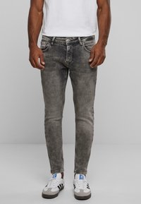 Jeans grises ajustados con textura deslavada y diseño de cinco bolsillos; combinados con zapatillas blancas con acentos en negro y gris.