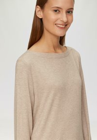 Beige langwerpige top met lange mouwen, gemaakt van een zachte stof met een brede bootnek. Heeft een relaxte pasvorm en minimale naden.