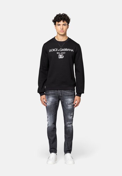 Zwarte katoenen sweatshirt met witte logoprint, gecombineerd met versleten grijze jeans en witte sneakers. Casual fit met geribbelde manchetten.