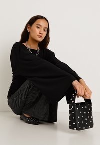 Mustast pikkade varrukatega pluus, laiad varrukad, triibulised püksid ja väike must käekott, mis on kaunistatud suurte hõbedaste naeltega. Väikesed madalad kingad täiendavad välimust.