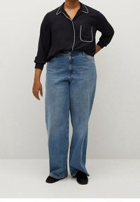 Sort langærmet skjorte med hvid piping og lomme, parret med højtaljede blå vidde jeans. Sorte sko fuldender outfittet.