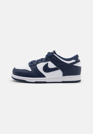 Zapatilla baja con paneles de cuero azul marino y blanco, cordones azul marino y suela de goma blanca con detalles azul marino.