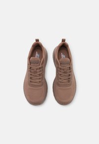 Brown athletic shoes made of knit material with a textured surface, featuring lace-up design, rubber sole, and pull tab on the heel.