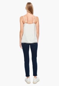 Witte top met dunne bandjes, getextureerde stof en kantafwerking aan de zoom, gecombineerd met donkere skinny jeans en witte sneakers.