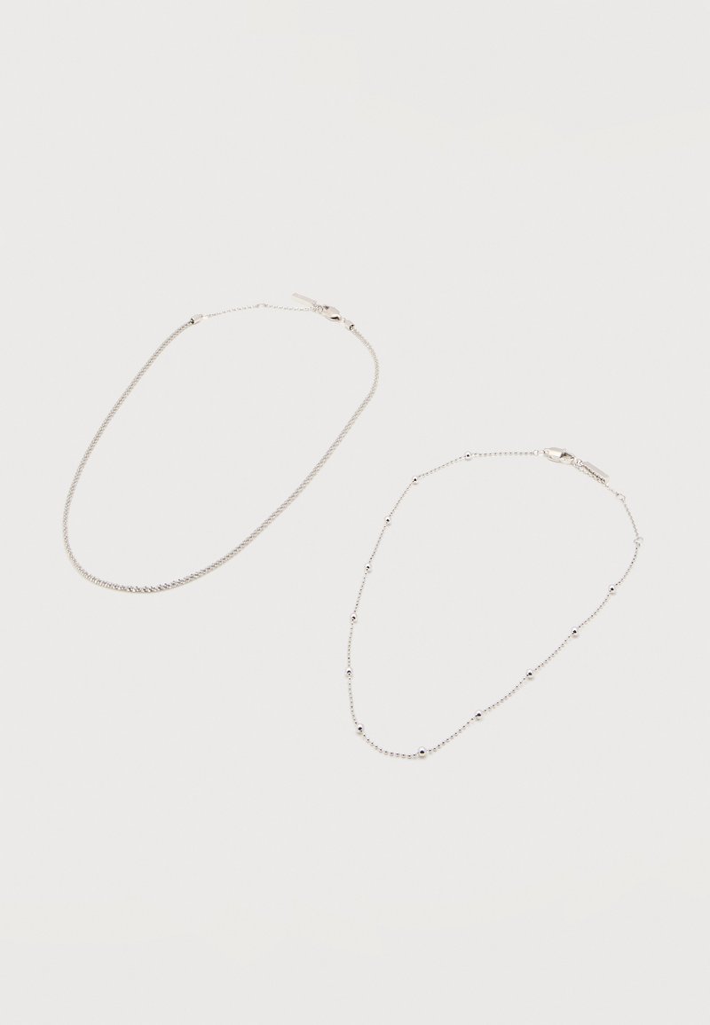 Δύο λεπτά βραχιόλια αλυσίδας από ασήμι με κούμπωμα καβουράκι· το ένα με μικρές στρογγυλές χάντρες τοποθετημένες ομοιόμορφα κατά μήκος της αλυσίδας.