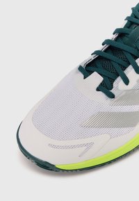 Chaussure de course avec une tige en mesh blanc, des lacets teal et une semelle vert lime. Comprend un design d'accent argenté sur le dessus.
