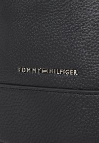 Black textured leather with a visible embossed "TOMMY HILFIGER" logo in silver metal. Features subtle stitching and smooth accents.
