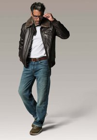 Veste bomber en cuir marron avec un col en fourrure, t-shirt blanc, jeans bleus et baskets marron. La veste comporte une poche poitrine et des poignets côtelés.