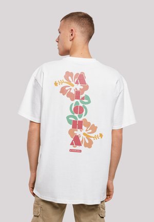 White cotton t-shirt featuring a colorful Hawaiian flower graphic and the word "ALOHA" in bold letters on the back. Short sleeves, relaxed fit.