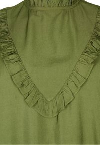 Grön tyg med en V-formad volangdetalj, rynkad vid halsringningen och kanterna, som visar struktur och sömnad.