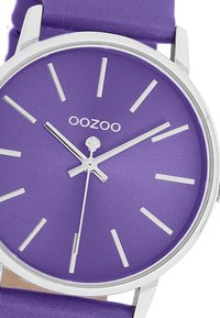 Purple silicone strap watch with a matte purple dial, silver hour markers, and logo. Circular stainless steel case with minimalist design.