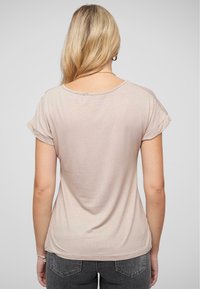 T-shirt beige clair avec des manches courtes à revers, un col large et une coupe décontractée. Le tissu semble doux avec un léger élasticité.