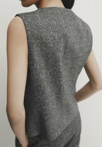 Harmaa hihaton paita, joka on valmistettu teksturoidusta kankaasta. Paidan pyöreä pääntie ja löysä istuvuus laskeutuvat tyylikkäästi olkapäiden yli.