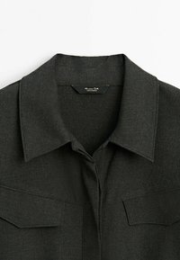 Dark gray shirt with a point collar, featuring two chest pockets and a smooth fabric texture. Label displayed at the neckline.