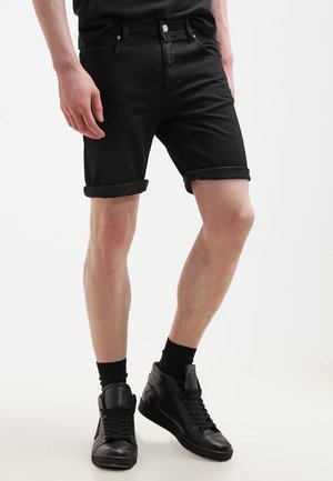 Shorts en denim noir avec des revers, dotés de poches avant et d'une coupe ajustée. Associés à des baskets montantes noires et des chaussettes noires.