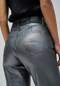 Jeans taille haute argent métallisé avec une texture lisse, dotés de deux poches arrière et d'une ceinture de marque noire.